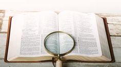 an open book with a magnifying glass on it sitting on top of a wooden table