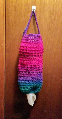 a colorful crocheted bag hanging on a wooden door with a tissue paper dispenser