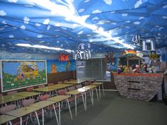 an empty classroom with many desks and paintings on the wall above them, under a blue tarp