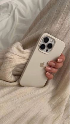 a woman's hand holding an iphone case on top of a white bed covered in blankets