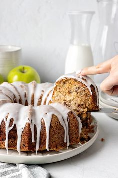 a person is cutting into a cake with white icing on it and apples in the background