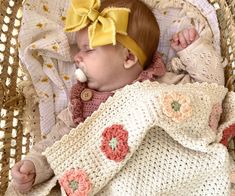 a baby laying in a basket with a yellow bow on its head and wearing a blanket