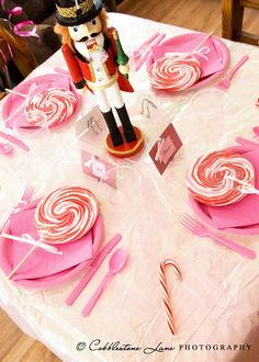 a nutcracker figurine sitting on top of a table with pink plates and candy canes