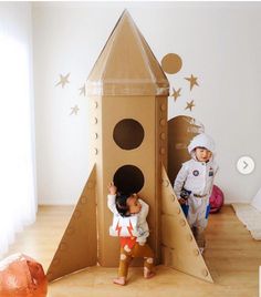 two children are playing in a cardboard rocket ship