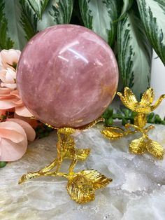 a pink marble with gold leaf accents on a rock next to some flowers and greenery