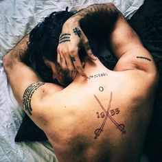 a man laying on top of a bed with tattoos on his back and arms behind him