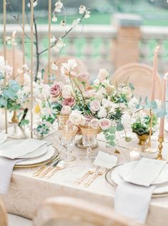 the table is set with white and pink flowers, gold place settings, and candles