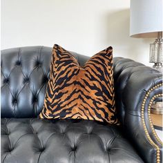 a tiger print pillow sitting on top of a black leather couch next to a lamp