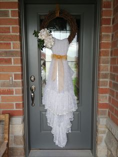 a dress hanging on the front door of a house with flowers and ribbon tied to it