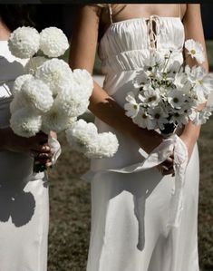 two women in white dresses holding bouquets of flowers