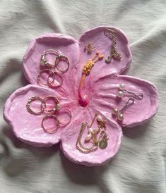 a pink flower shaped tray with rings and other jewelry on top of white cloths