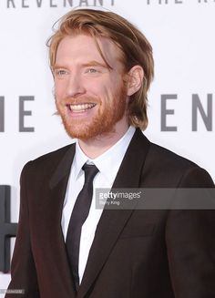 a man in a suit and tie smiles at the camera while standing on a red carpet