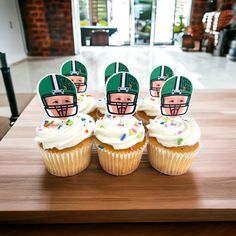 four cupcakes with football helmets on them sitting on a wooden table in front of a window