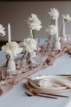 the table is set with white flowers in vases and place settings, along with silverware