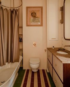 a white toilet sitting next to a bath tub in a bathroom under a framed painting