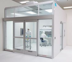 two people in white lab coats are standing near the glass doors to an operating room