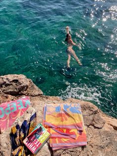 a woman swimming in the ocean next to some towels and other items that are laying on rocks