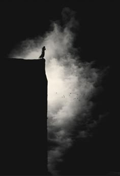 a person standing on top of a tall building in the dark with clouds behind them