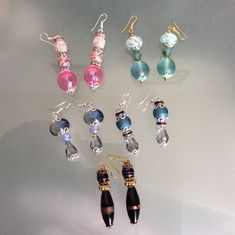 six pairs of earrings are displayed on a white surface, including one black bead and one pink bead