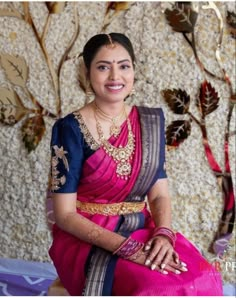 a woman in a pink and blue sari sitting on a bed with flowers behind her