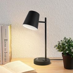 a black lamp sitting on top of a wooden table next to a book and potted plant