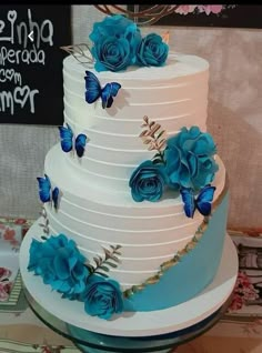 a three tiered cake with blue flowers and butterflies on the top is sitting on a table