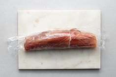 a piece of meat wrapped in plastic sitting on top of a white marble countertop