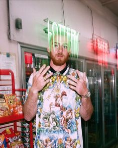 a man standing in front of a store holding his hands up to the camera while wearing a shirt with images on it