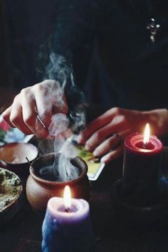 a person lighting candles on a table with other items around it and another candle in the foreground