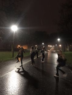 some people are skateboarding on a wet road at night