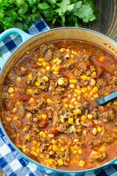 a blue pot filled with meat and corn on top of a checkered table cloth