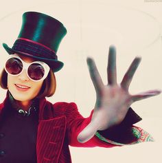 a woman wearing sunglasses and a top hat with her hand up in the air,