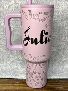 a pink travel mug with the word sullie on it and various items around it