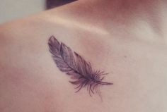 a woman's chest with a small feather tattoo on it