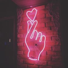 a neon sign with a hand holding a heart on it's side in front of a brick wall