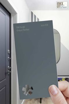 a person holding up a gray paint swatch in front of a door and mirror