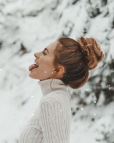 a woman standing in the snow with her mouth open and looking up at something behind her