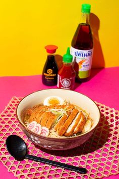 a bowl of food on a pink place mat with spoons and condiments