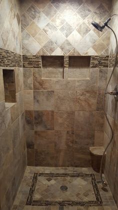 a walk in shower sitting next to a tiled wall and floor covered in brown tile