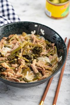 a bowl filled with meat and vegetables next to chopsticks on a marble counter