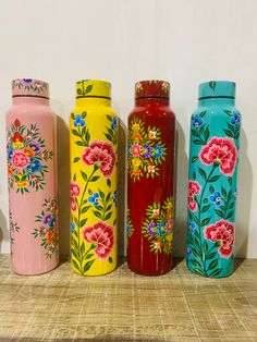 four colorful vases are lined up on a shelf next to each other and one has flowers painted on it