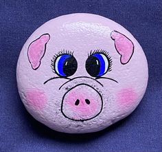 a painted rock with a pig face on it's side, sitting on a blue surface