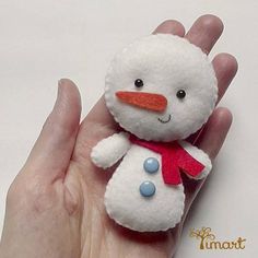 a hand holding a small white snowman with red scarf on it's head