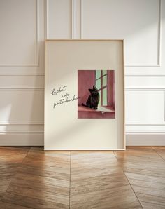 a black cat sitting on top of a wooden floor next to a white frame with the words be what you are looking for