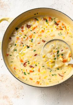 a large pot filled with soup on top of a white countertop next to a wooden spoon