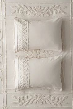 three pillows and two pillow cases on top of a white quilted bed spread with embroidered trim