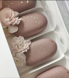 three pink and gold decorated donuts in a white box with flowers on the top