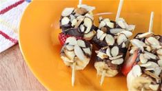 chocolate covered strawberries and bananas on skewers sitting on an orange plate next to a napkin