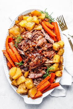 a white plate topped with meat, potatoes and carrots next to a knife and fork