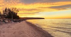 the beach is lined with rocks and trees as the sun sets